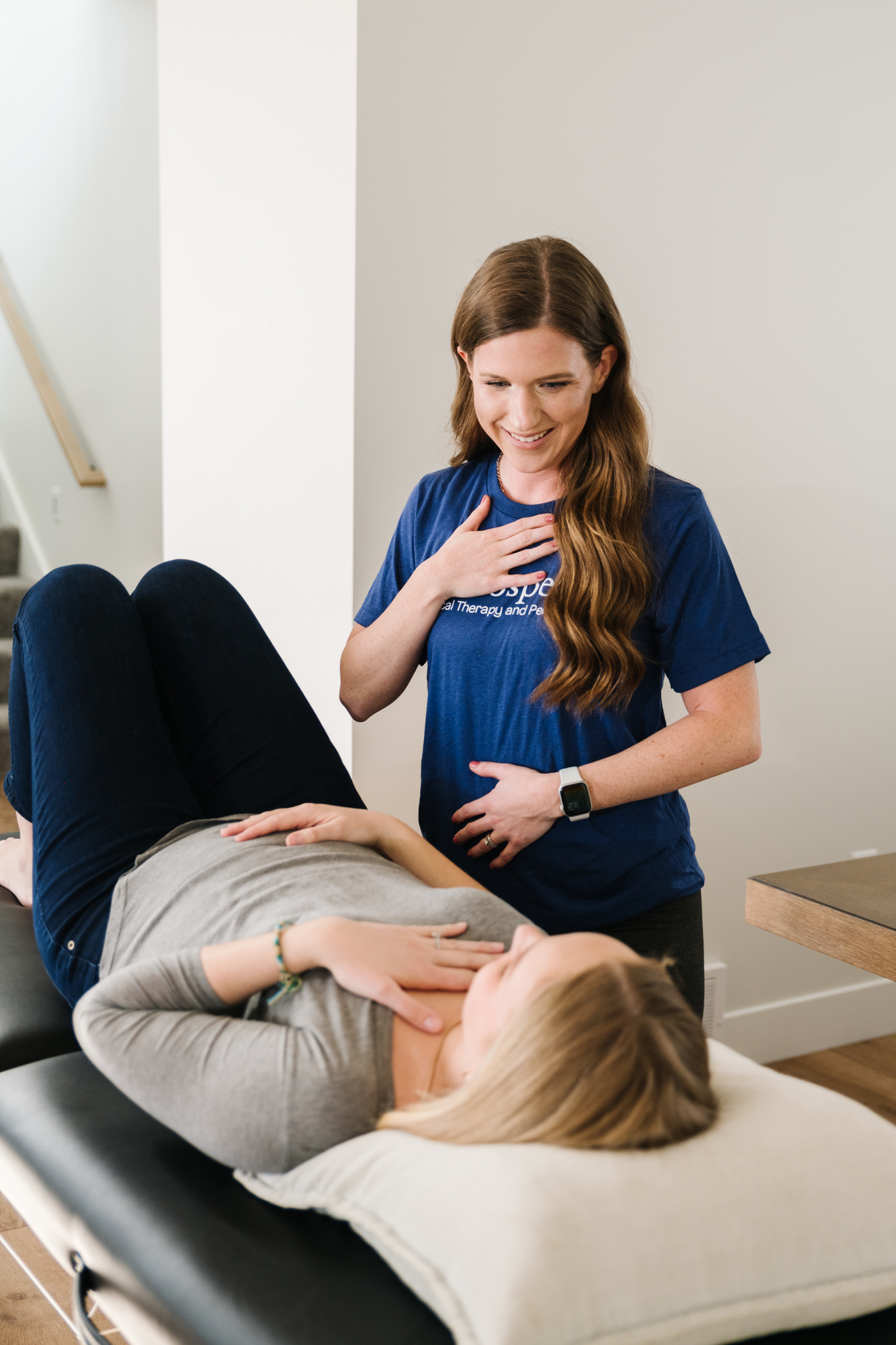 Image of therapist demonstrating diaphragmatic breathing to a patient who is pregnant while she is laying on her back.
